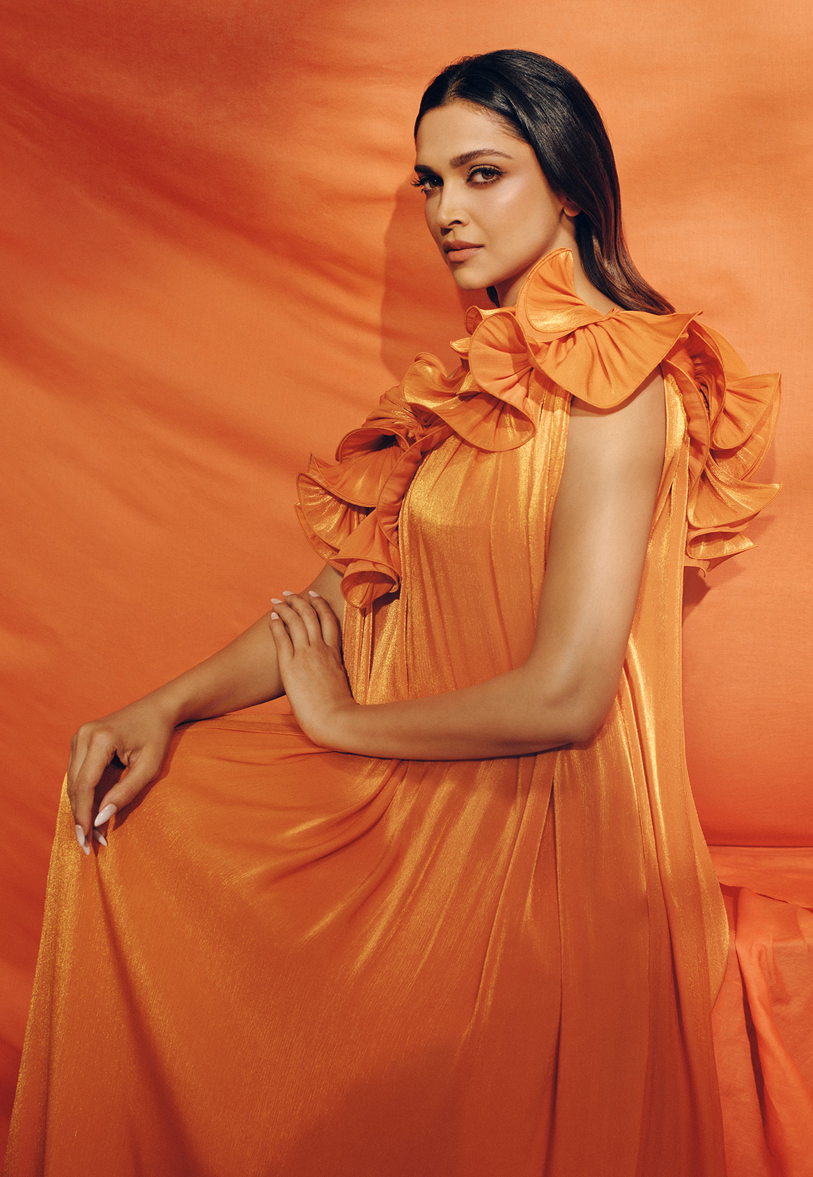 deepika padukone wears an orange silk dress and poses against an orange fabirc backdrop