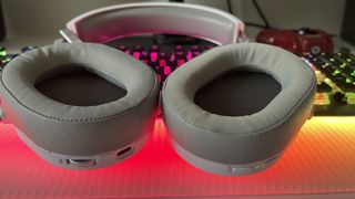 Corsair HS65 Wireless gaming headset open to show interior of cups on a desk with a keyboard in the background