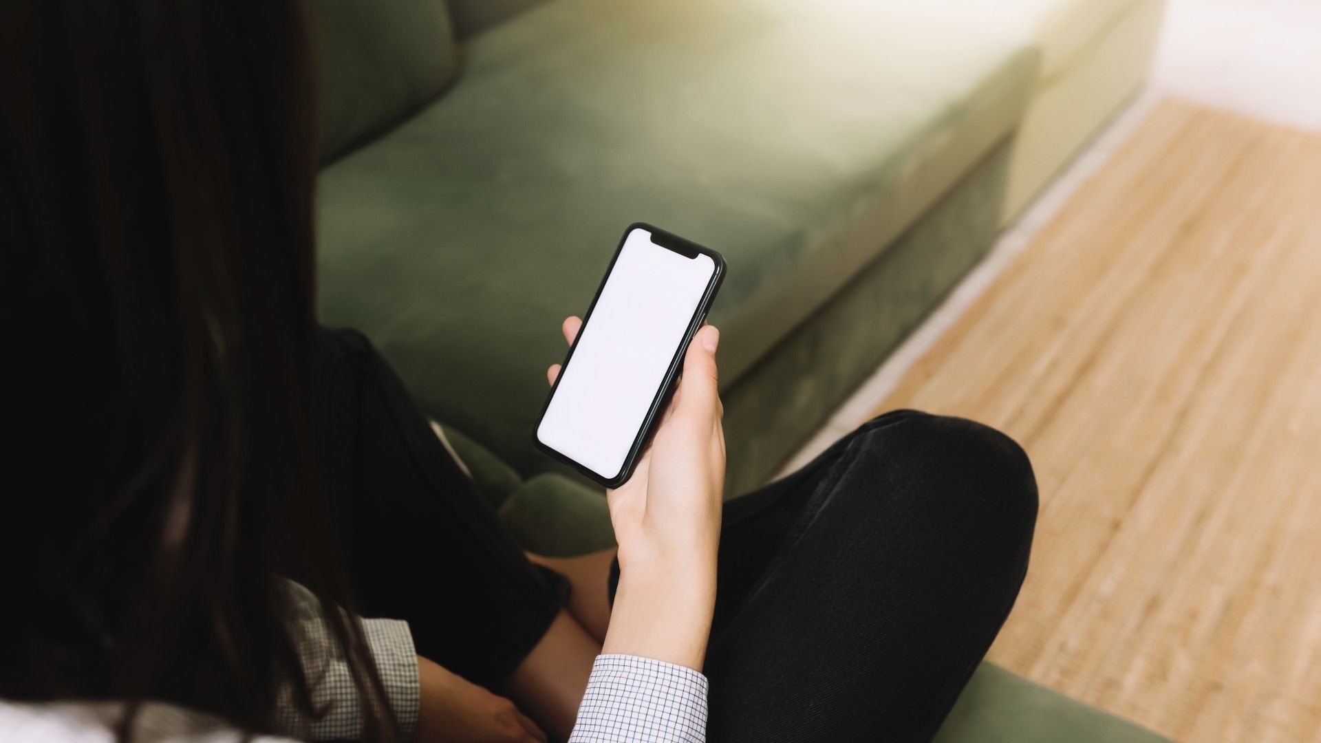 person holding a mobile phone whilst sat on a green sofa