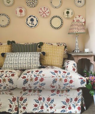 living room with patterned floral sofa and lots of cushions and plates on wall with sidetable and patterned lamp