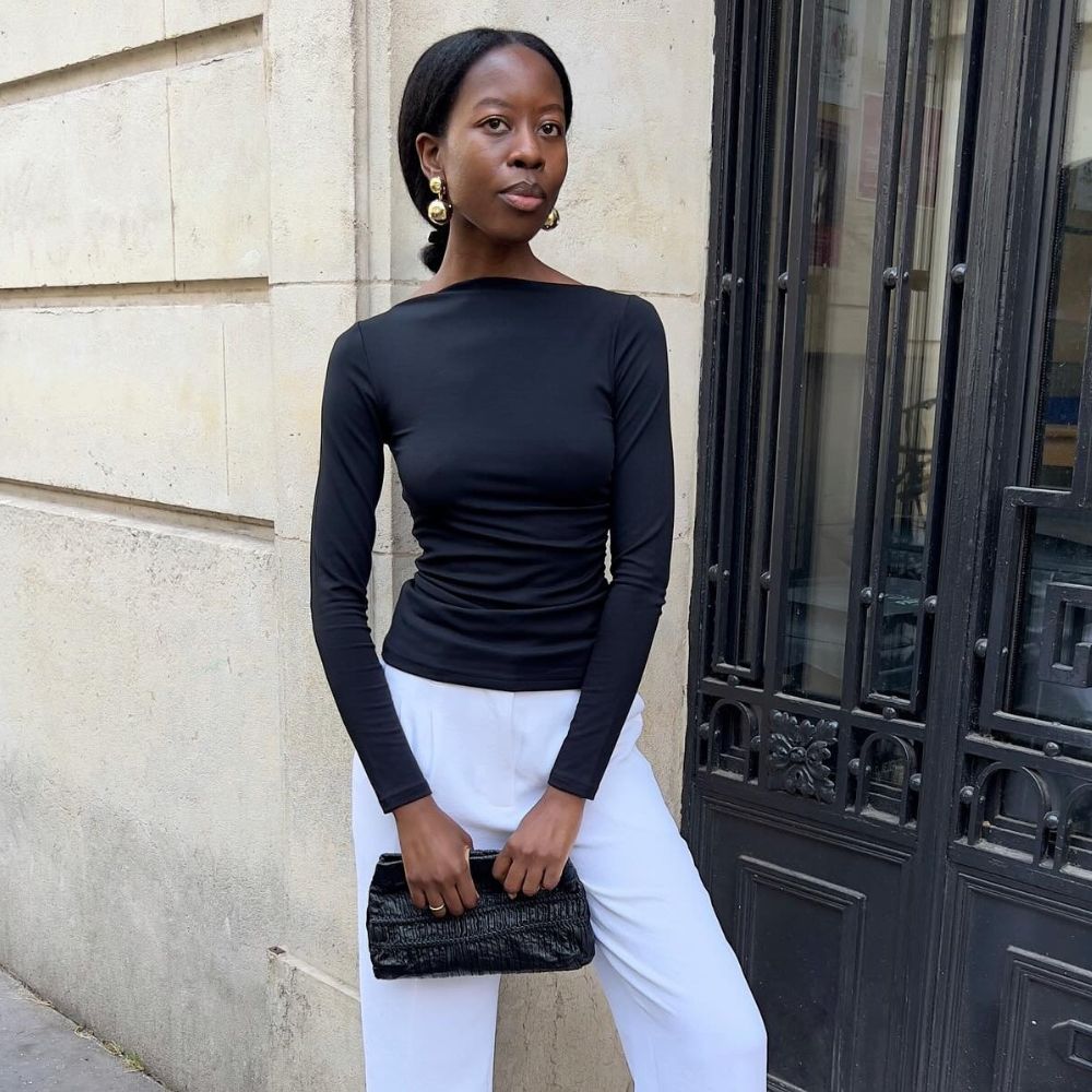 French influencer @sylviemus_ stands on the street in Paris wearing a black boat neck top with white cropped trousers.