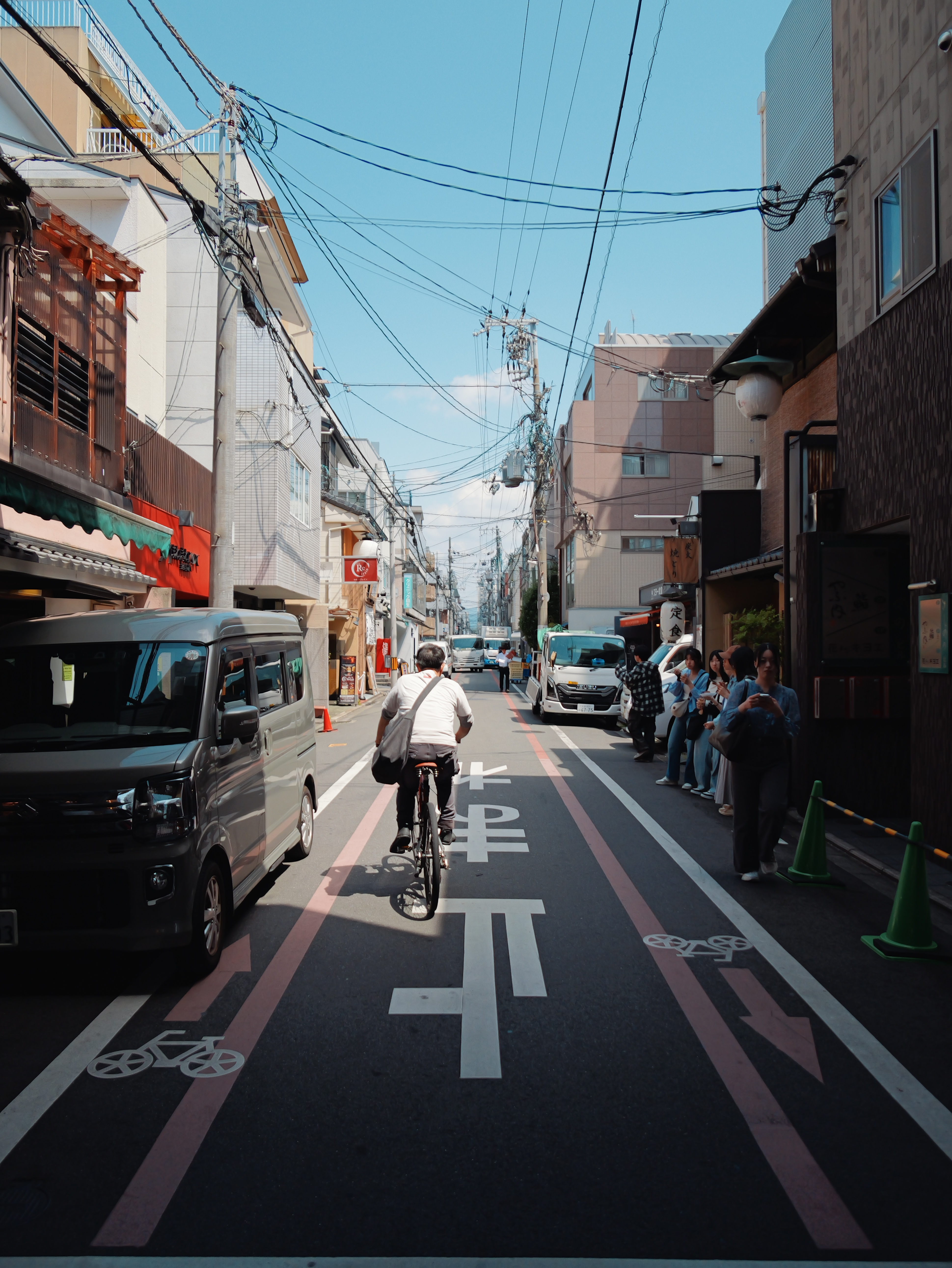 Cyclist riding along a narrow Japanese street under overhead cables.