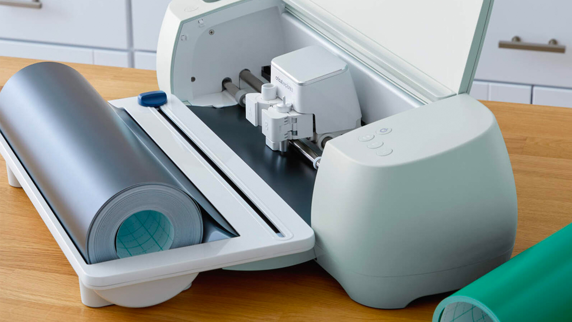 A Cricut craft machine on a table with rolls of material