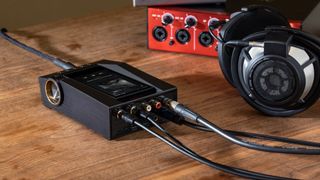 The Astell&Kern CA1000T on a wooden surface with cables plugged into it, in front of a pair of over-ear headphones.