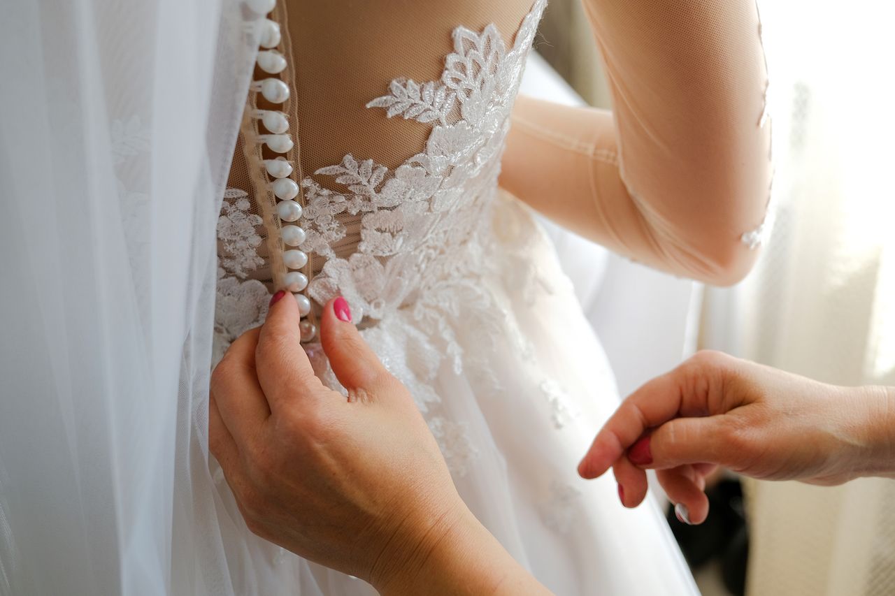 Wedding diet: Mom laces up the back of her daughter&#039;s openwork stylish wedding dress. Morning Preparations of the bride, support and care of the mother.