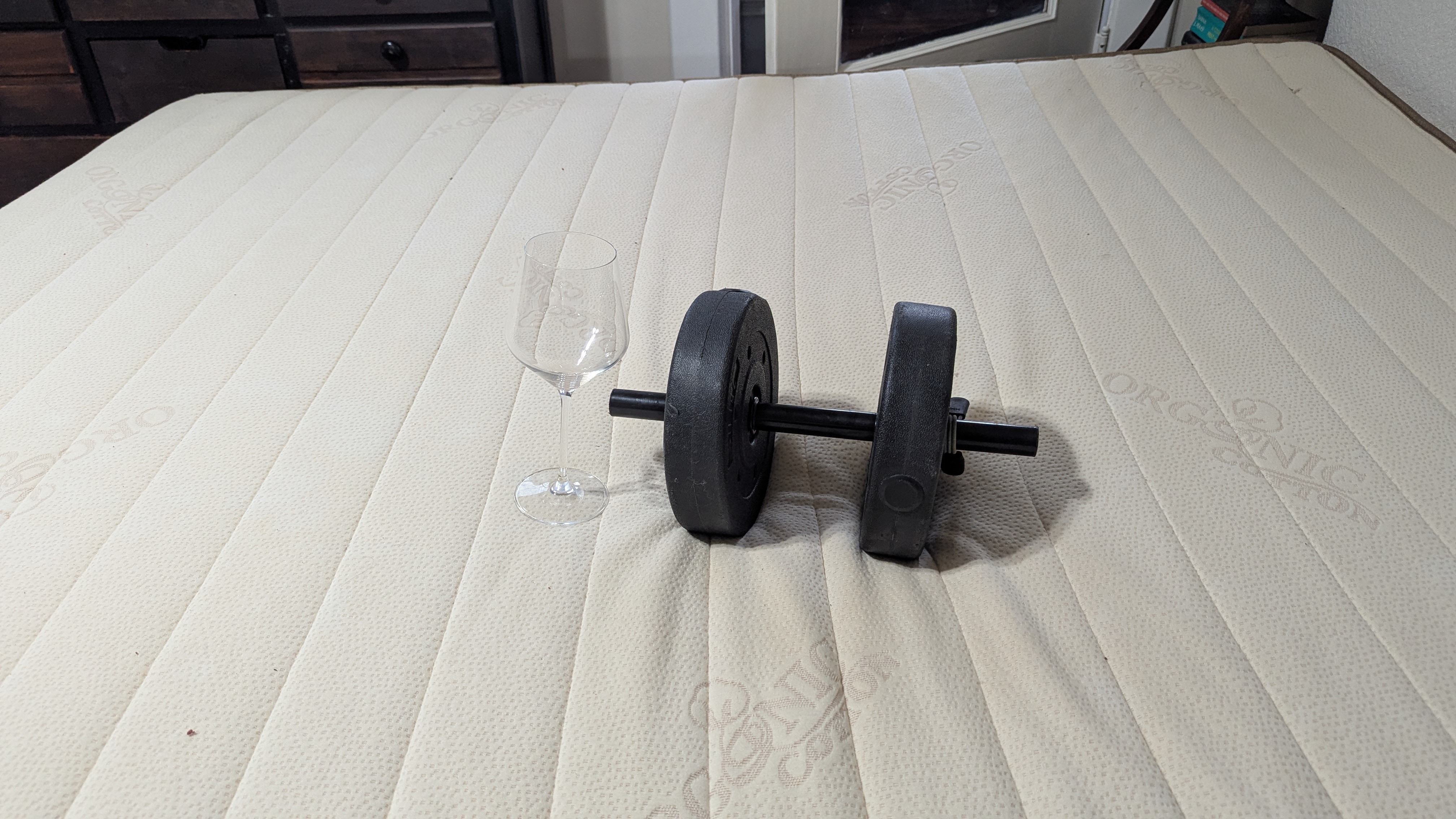 A dumbell next to a wine glass on top of the mattress to prove the excellent motion isolation of the Plushbeds Botanical Bliss mattress