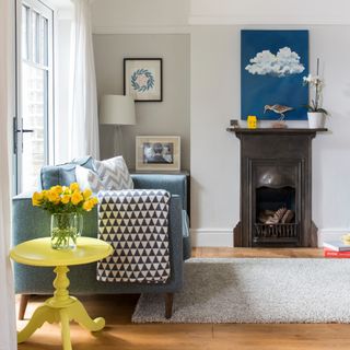 A living room with a contrasting small black fireplace, a blue sofa to the side and a yellow side table