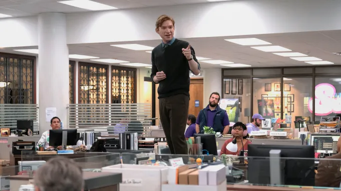 Domnhall Gleeson stands on a desk in The Paper
