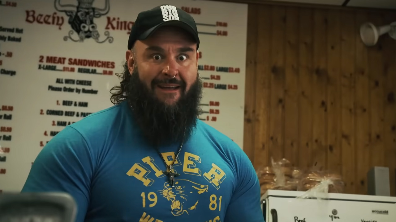 Braun Strowman in a blue t-shirt and baseball cap excited about food and staring straight at the camera on Everything on the Menu. 