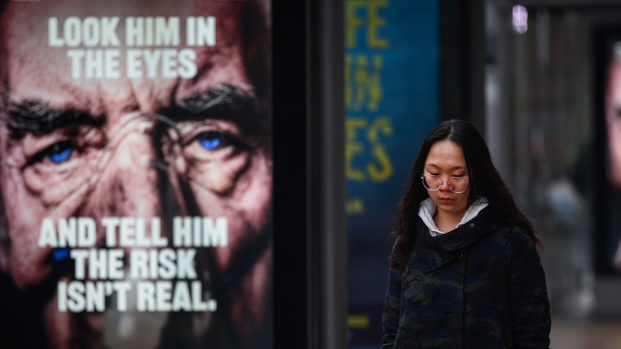 A member of the public walks past a Covid warning advert.