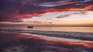 Beach scene, colourful sunset and impactful clouds getting mirrored in the water
