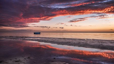 Beach scene, colourful sunset and impactful clouds getting mirrored in the water