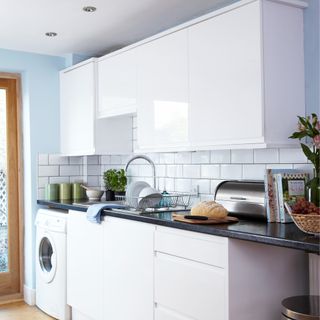 A white glossy kitchen with a washing machine and a dish rack