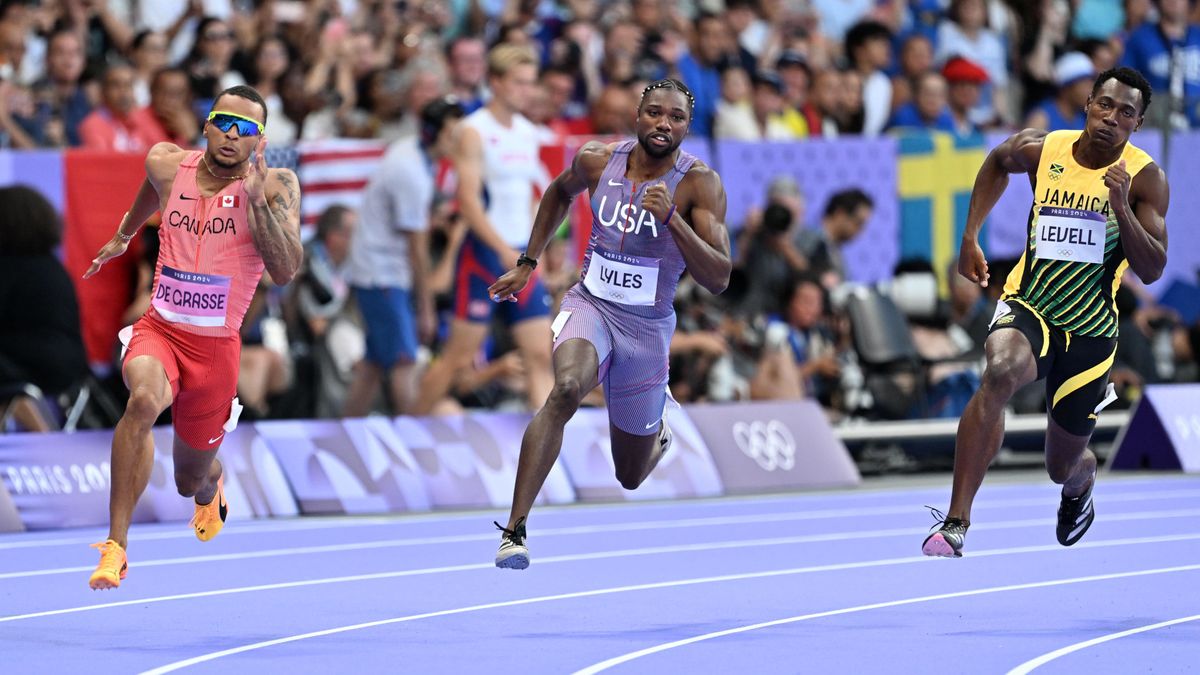 Noah Lyles (C), in a blue and red fine-striped running suit, runs the bend in the men&#039;s 200m at the 2024 Paris Olympic Games.