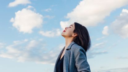 A woman leans her head back and takes a deep, cleansing breath against the backdrop of a beautiful blue sky.