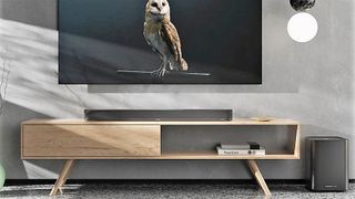 front-on image showing Sennheiser Ambeo Soundbar Plus on wooden surface beneath a TV screen