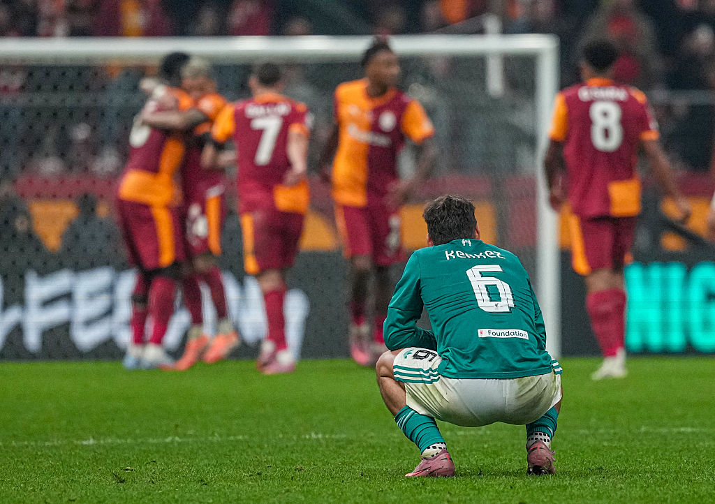 Milos Kerkez squats, dejected, as Galatasaray celebrate in their victory over Liverpool