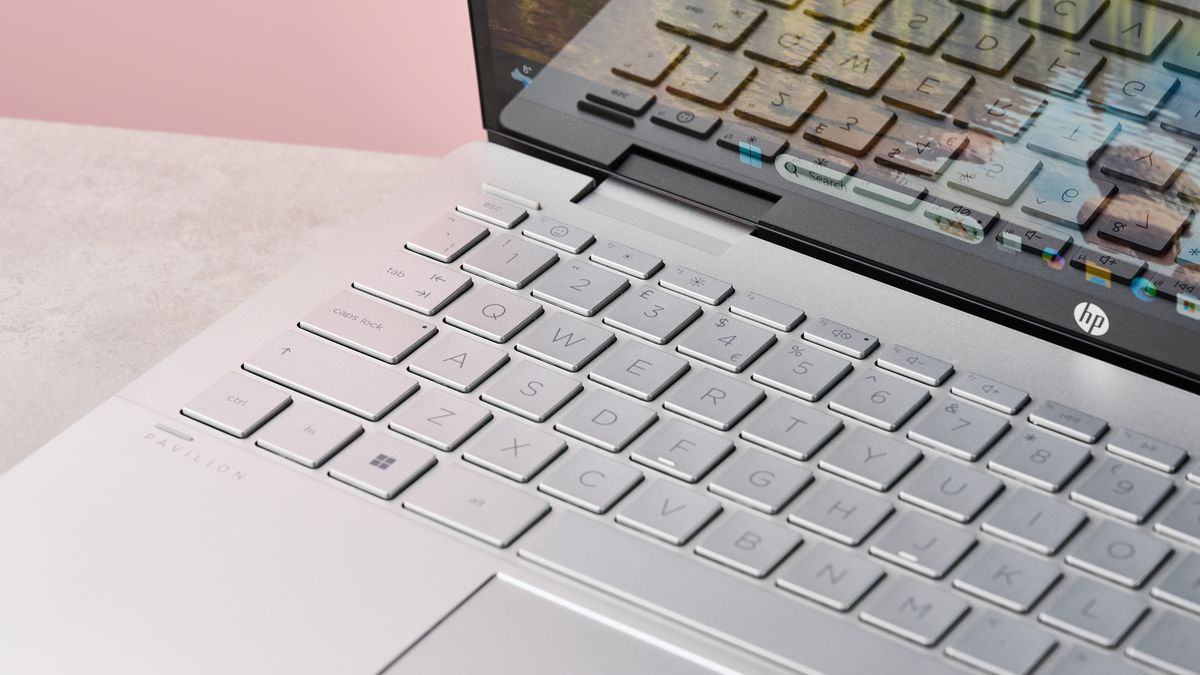 Close-up of keyboard on HP Pavilion x360 14, with desk and pink wall in background