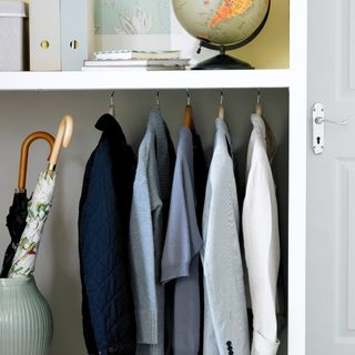 Open shelving next to a living room door fitted with a tension rod to hanf a few jackets and shirts next to a umbrella holder