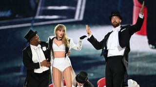 From left to right: Kam Saunders holding up Taylor Swift who is looking at Travis Kelce, who has both his arms raised. This image was taken at the Eras Tour at Wembley Stadium on June 23, 2024.