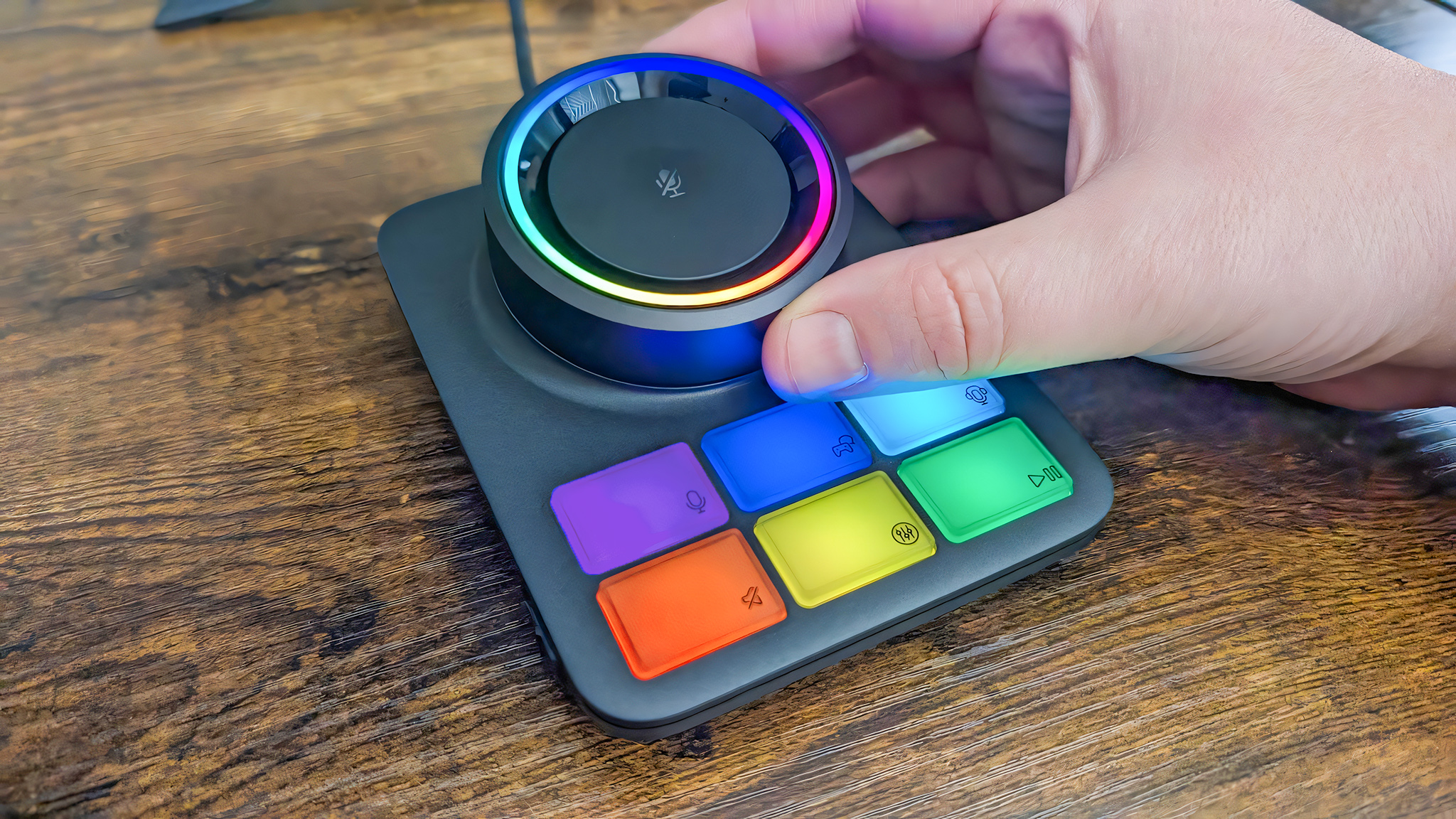 A close-up of the RGB Base Station with lighting on. A hand rotates the large volume dial.