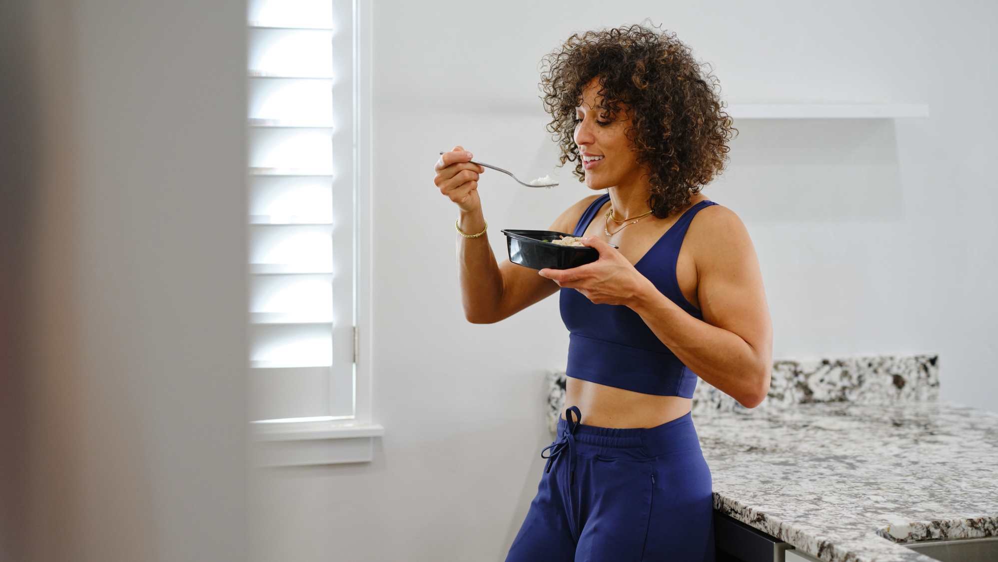 Woman in sportswear eating from a bowl with a spoon