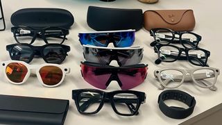 Three Oakley Meta HSTN, three Oakley Meta Vanguard, and three Ray-Ban Meta (Gen 2), along with cases, sitting atop a table in various styles, along with the Meta Ray-Ban Display glasses in front of them all.