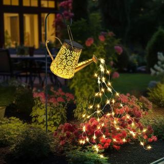 A watering can-shaped metal container filled with string lights in a garden