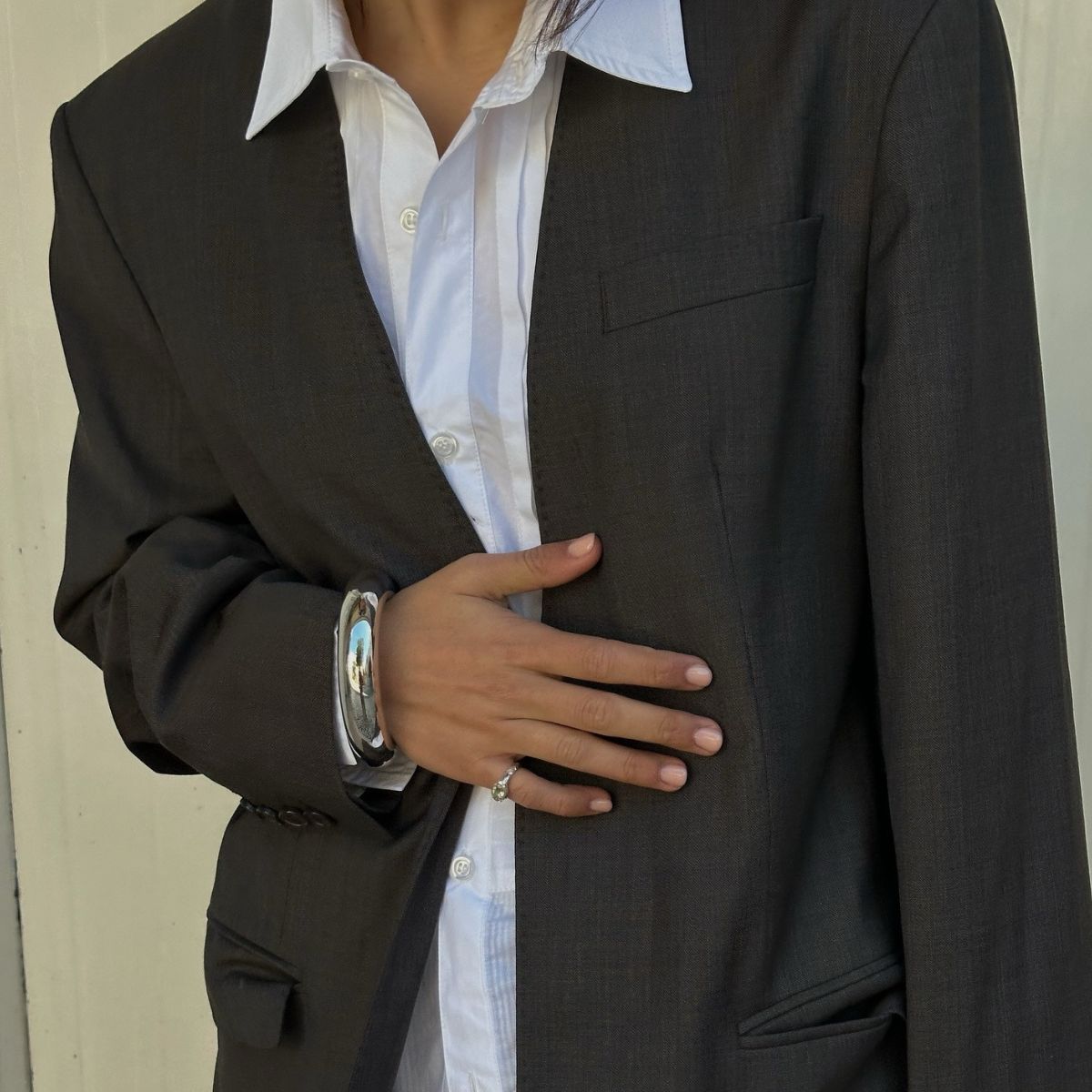 A close-up of a women's outfit, including a white shirt, a grey blazer and a silver bangle