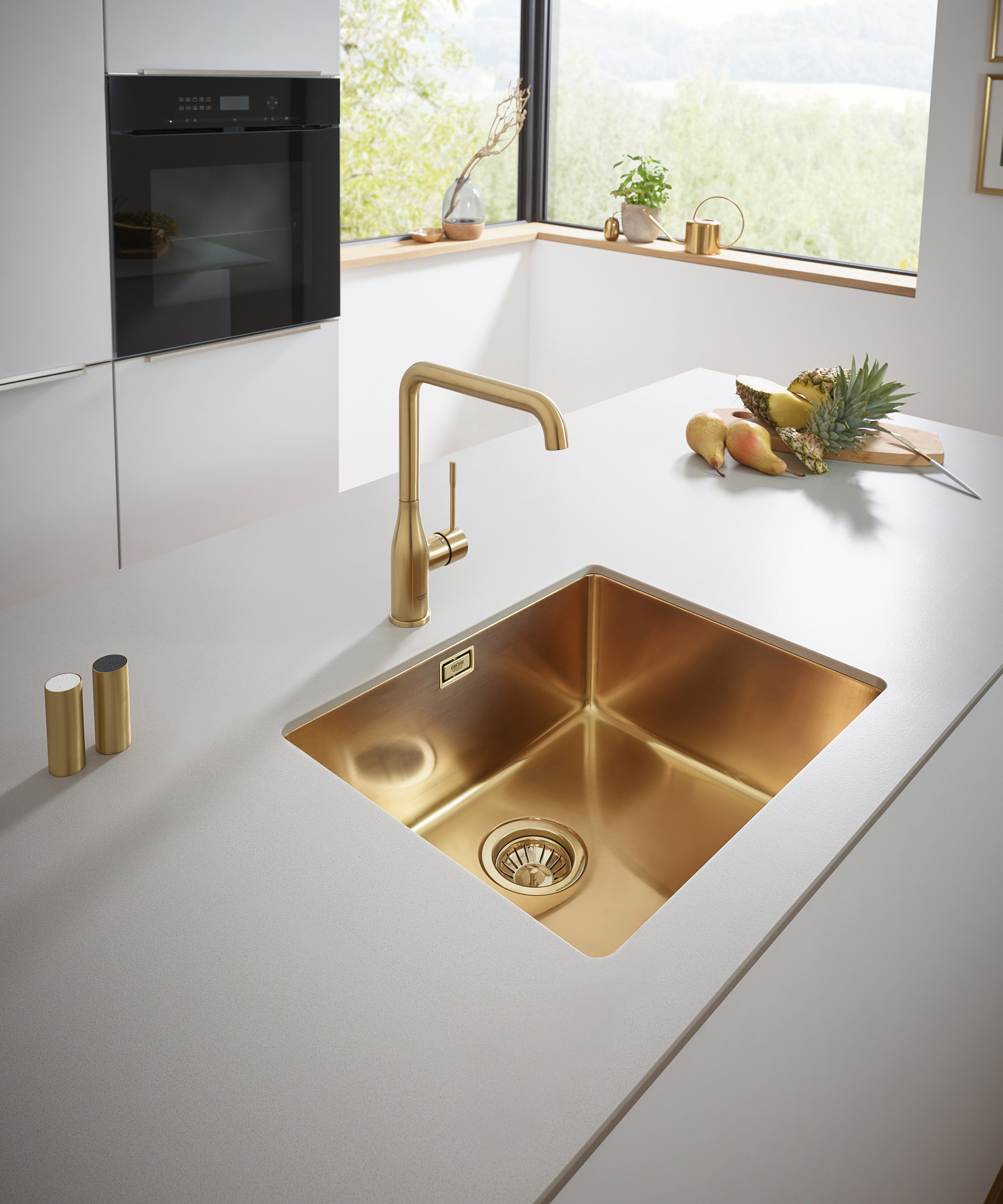 A closeup of a minimalist white island worktop with a gold faucet and sink