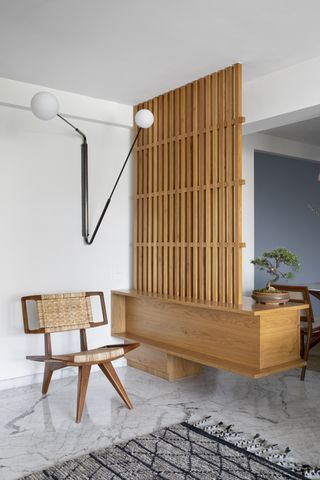 A small living room with a lighting piece on the wall, highlighting a wooden screen