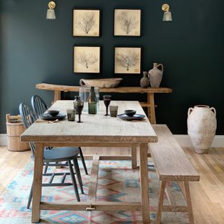blue dining room with rustic matching table, bench, console, two dark grey chairs, vintage style rug, artwork, wall lights, earthenware pots, black tableware