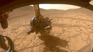a mars rover's robotic arm investigates a bright, dusty rock on the red planet