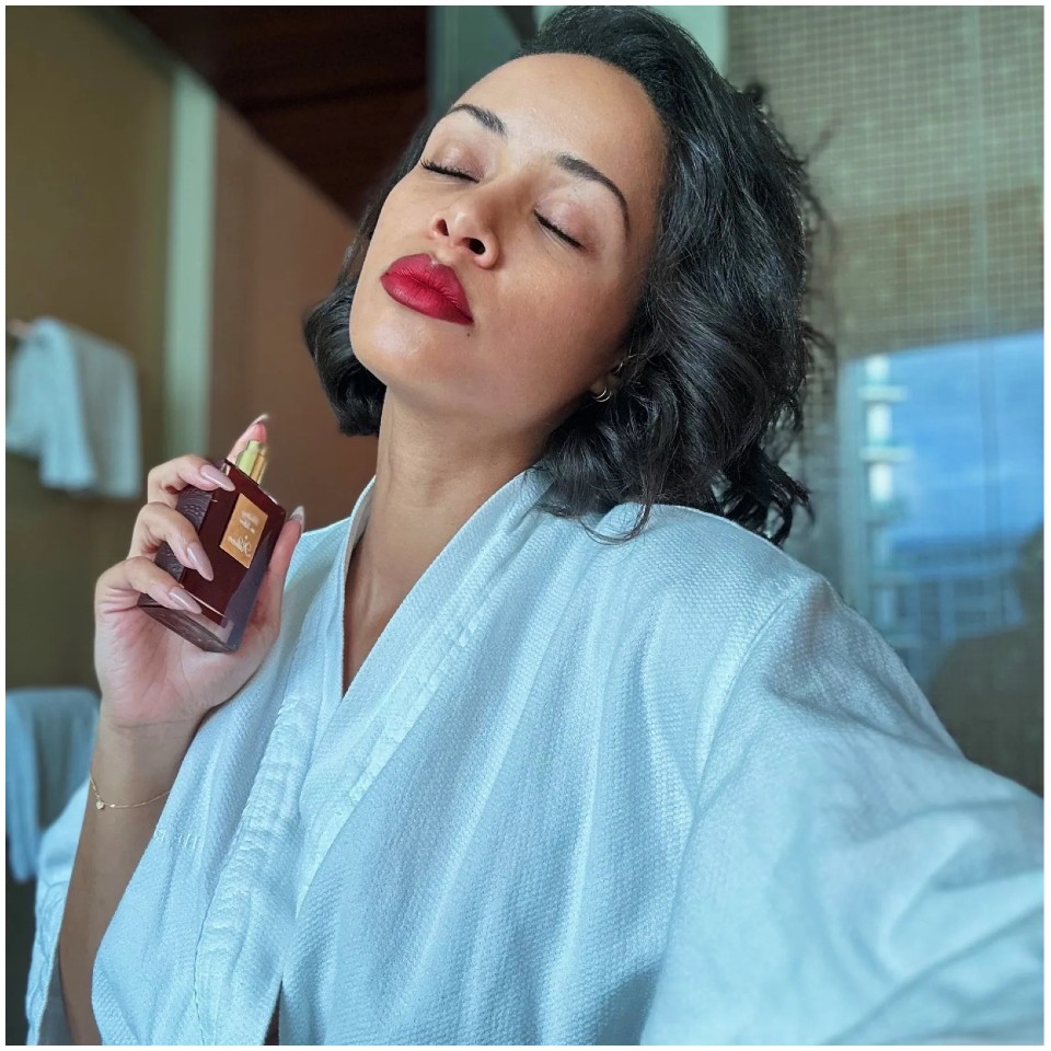 An image of a woman with red lipstick holding a red perfume bottle