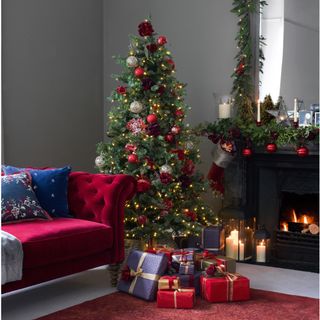 Christmas tree with red and purple presents underneath next to red sofa on red rug