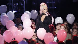 Christina Aguilera sings on stage surrounded by fans and balloons.