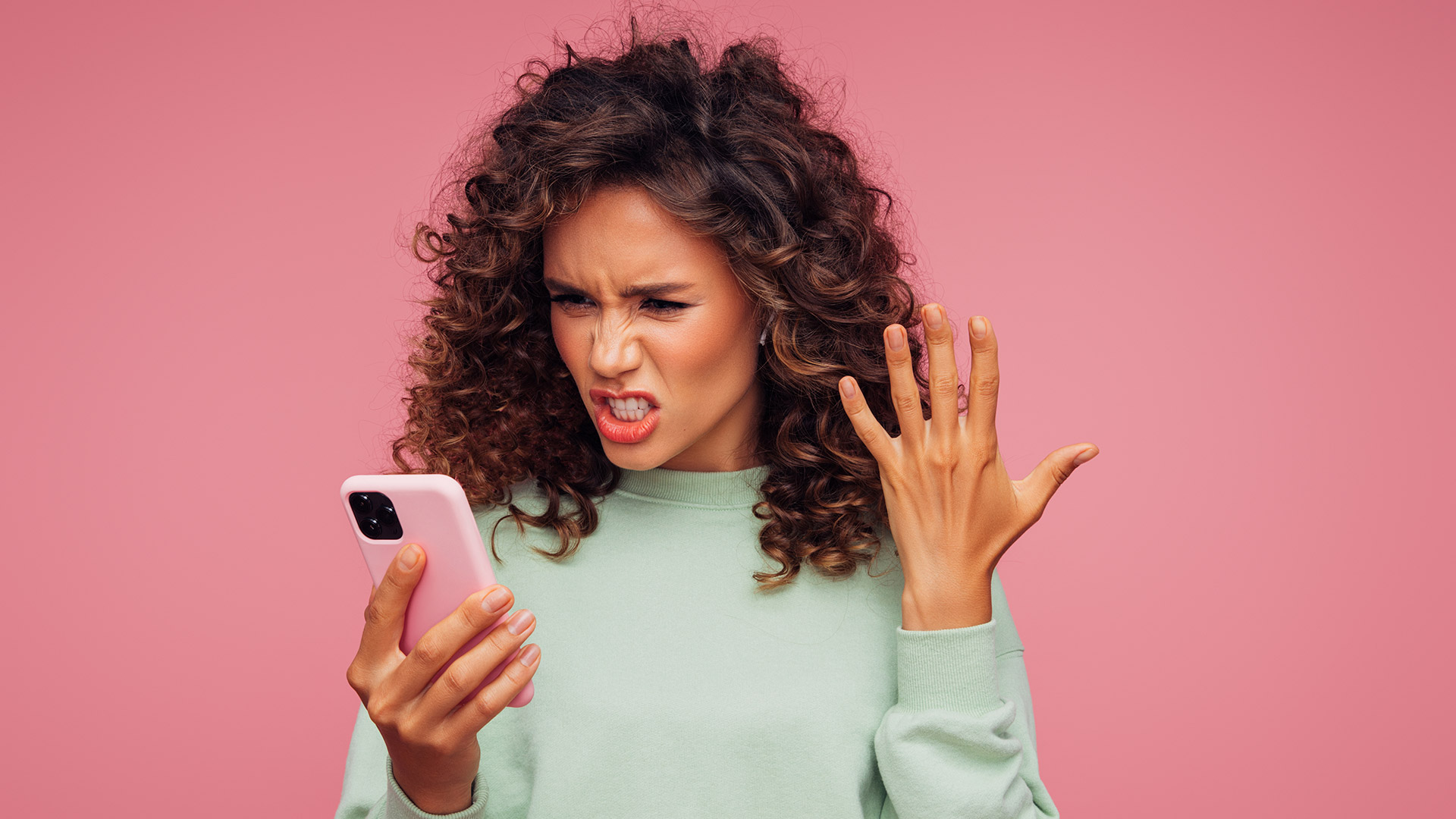 A woman looking angrily at a phone screen, on a pink background