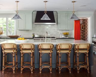 kitchen with light green upper cabinets, gray-blue kitchen island with white countertops, and five woven bar stools