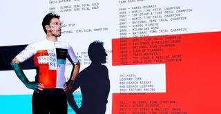 Fabian Cancellara in a white and red patterned jersey in front of a screen projecting his greatest victories 