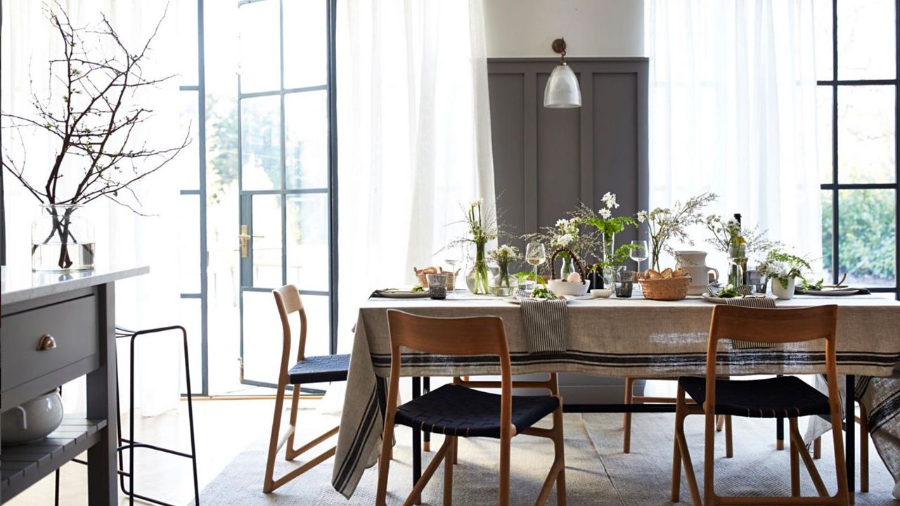 Grey and white dining room with retro chairs and table with tablecloth laid with spring flower displays