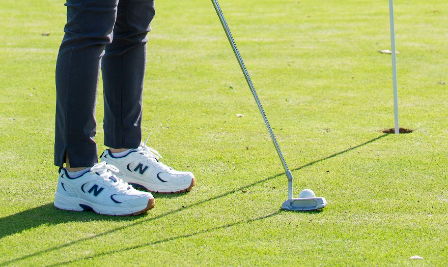 A golfer putting with New Balance shoes on