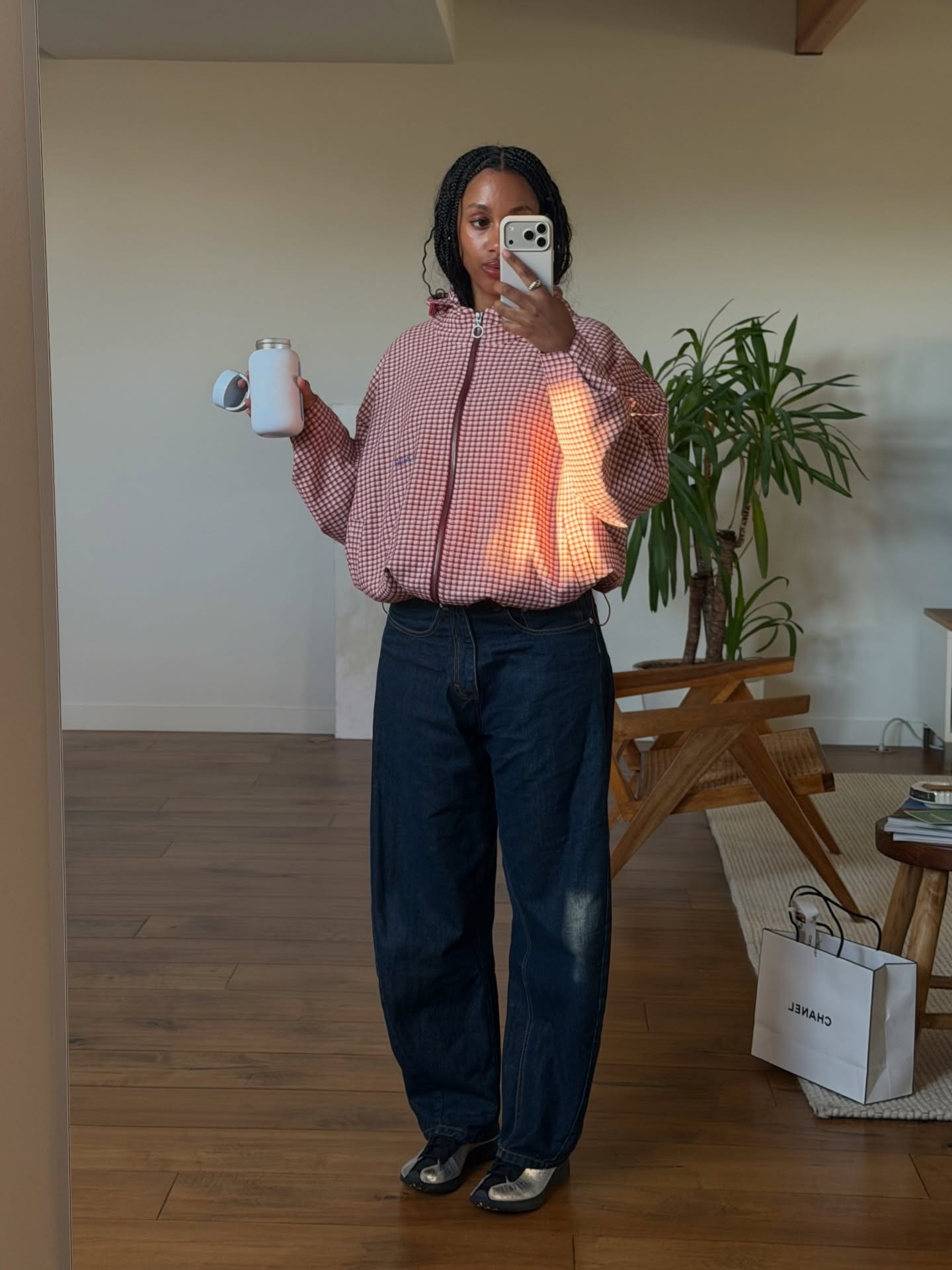 @claire_most wearing a plaid bomber jacket with dark-wash barrel jeans and sneakers.