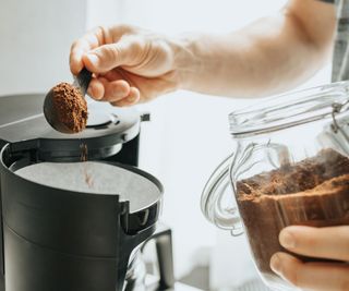 A man adding freshly ground coffee to the top of a drip coffee maker