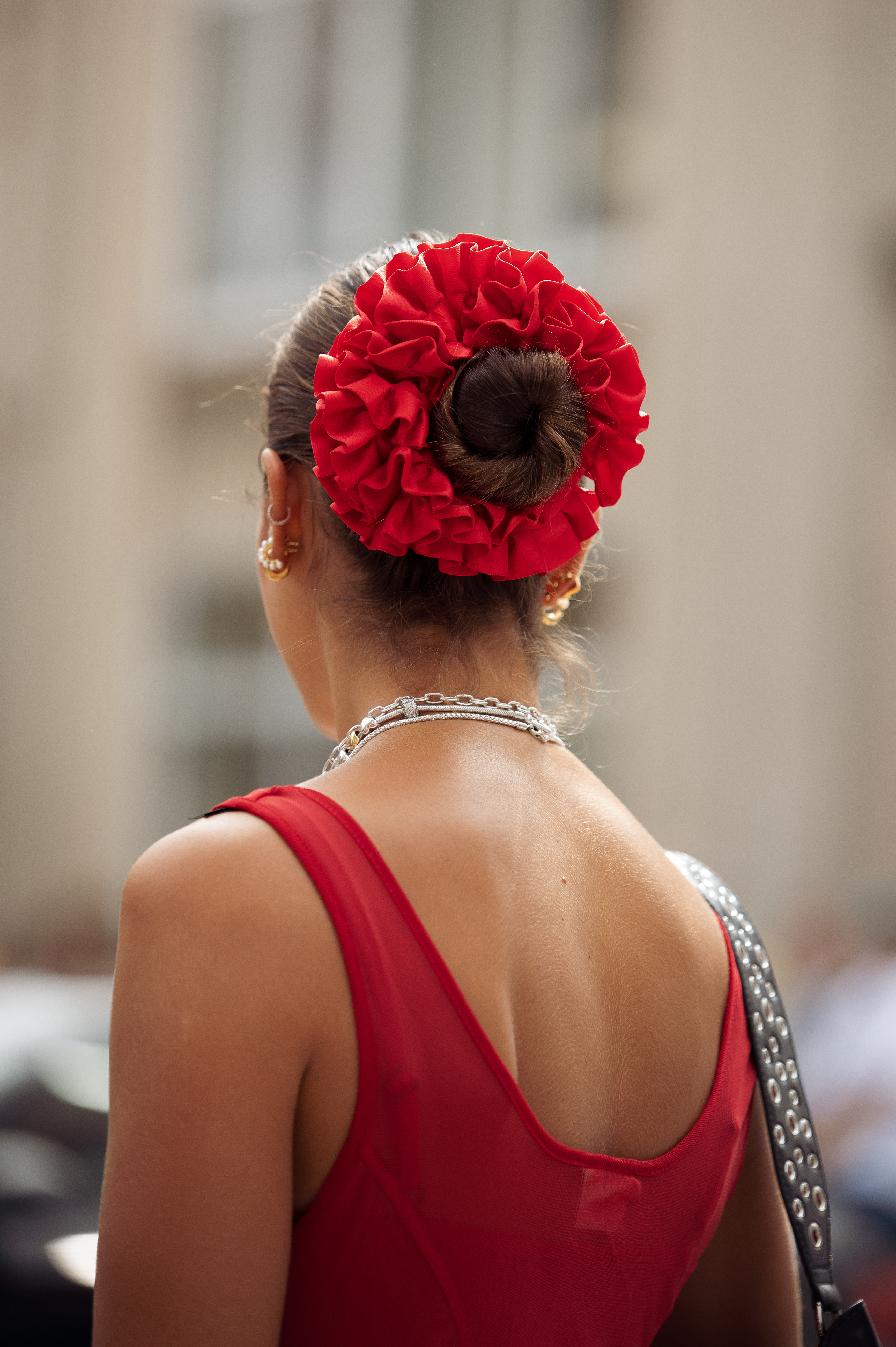 person with a slicked back bun wearing a bright red oversized scrunchie around the bun