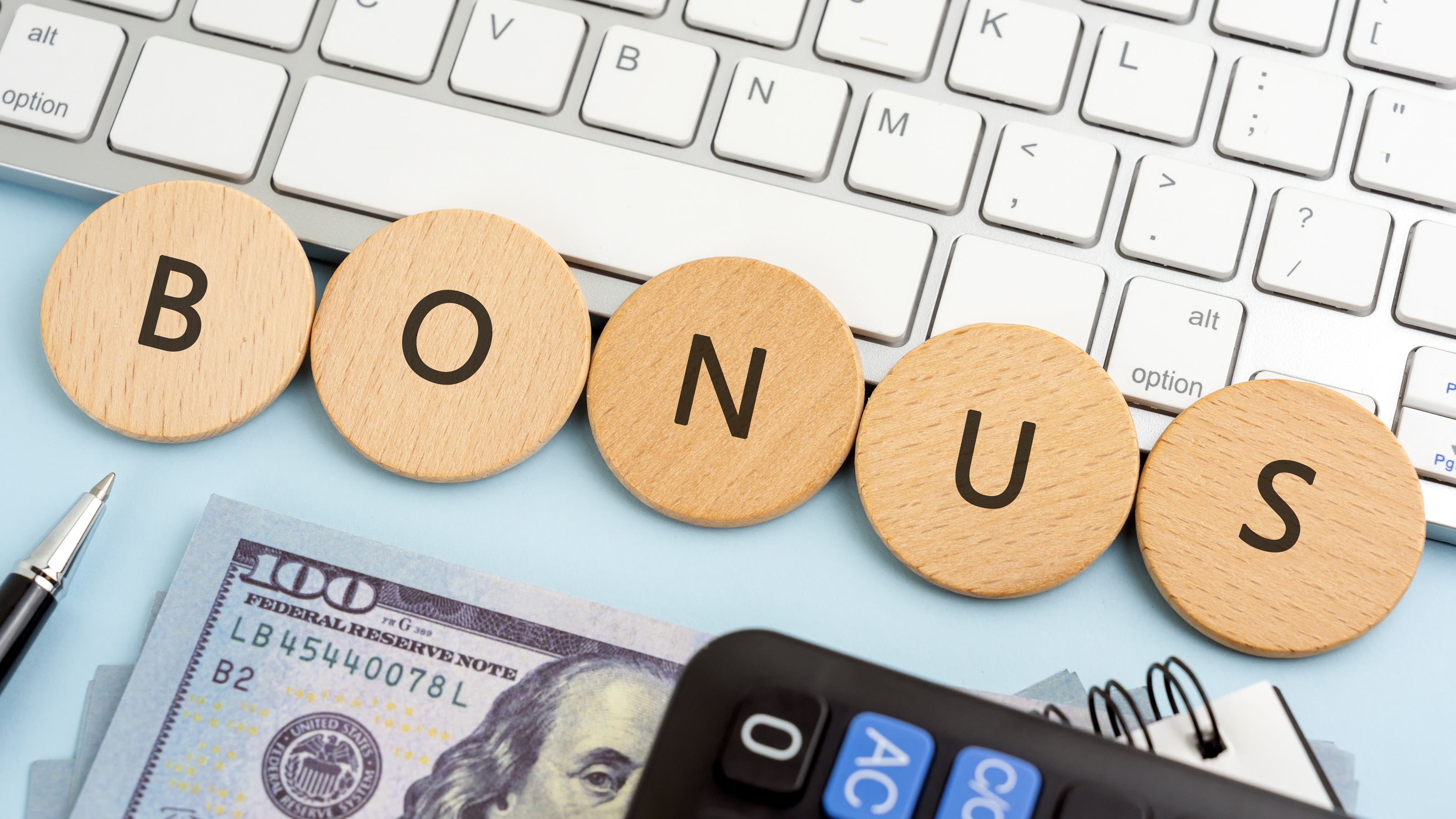 The word &quot;bonus&quot; spelled out on round wooden plates next to a keyboard, money and calculator.