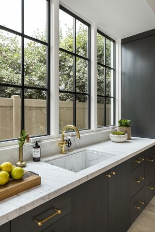 kitchen with dark blue cabinets, brass handles, marble worktop and large windows