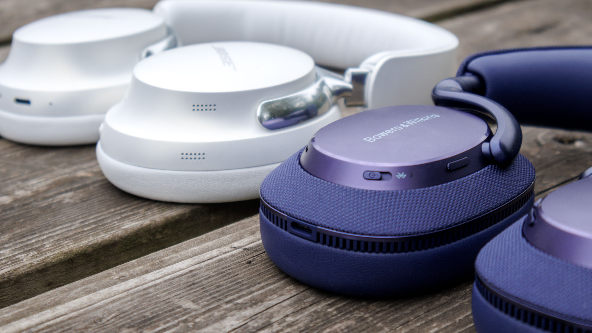Bowers & Wilkins Px7 S3 vs Bose QuietComfort Ultra Headphones on a wooden surface, closeup of the controls