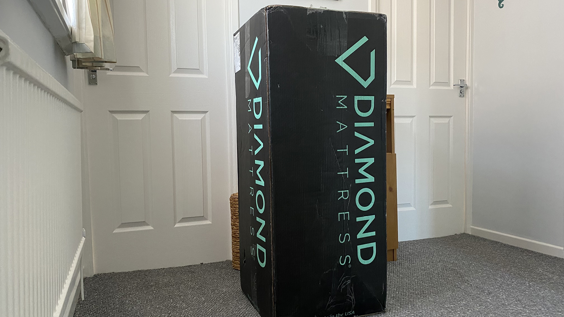 The Dreamstage Value Quilted Hybrid Mattress upright in its Diamond Mattress in our reviewer's hallway, either side of two closed doors