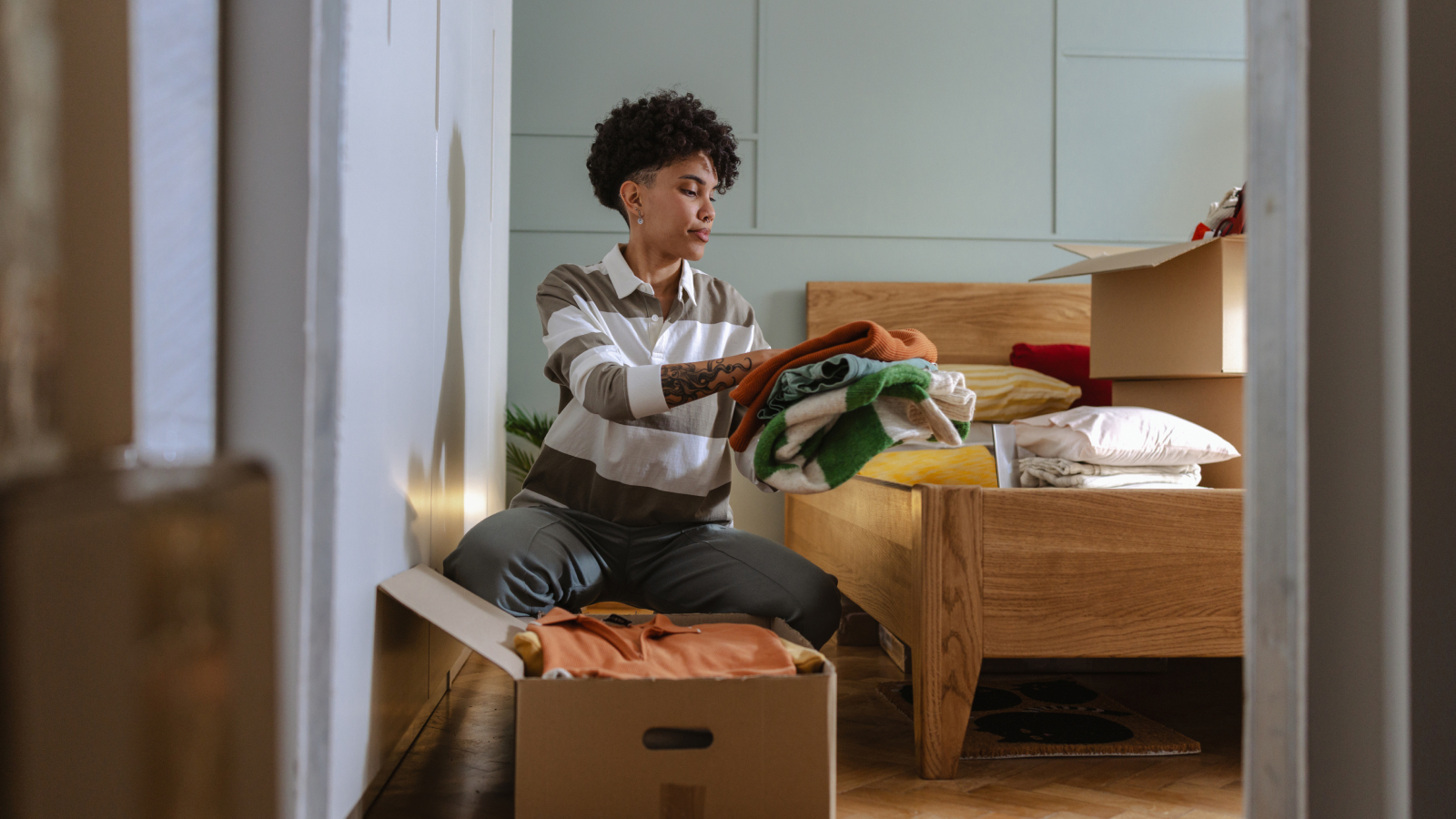 woman sorting out piles of clothes in cardboard boxes in bedroom