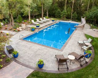 swimming pool with slide, basketball hoop, and patio with loungers